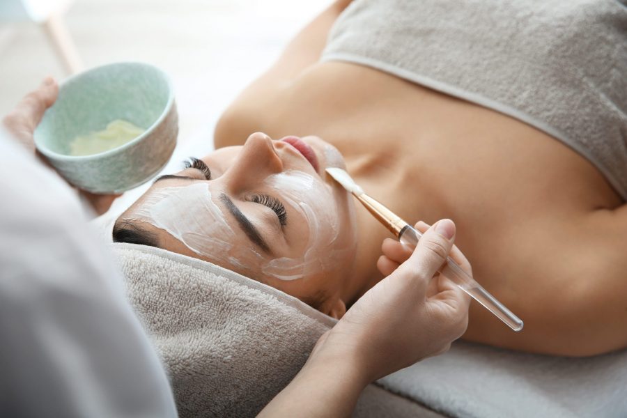 Cosmetologist applying mask on client's face in spa salon